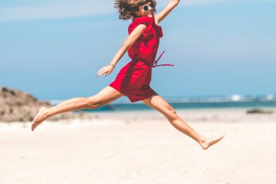 Kvinde hopper på strand fordi hun er glad