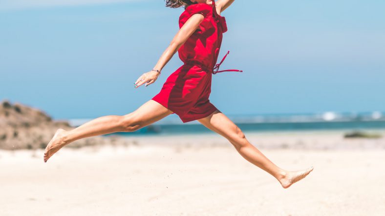 Kvinde hopper på strand fordi hun er glad